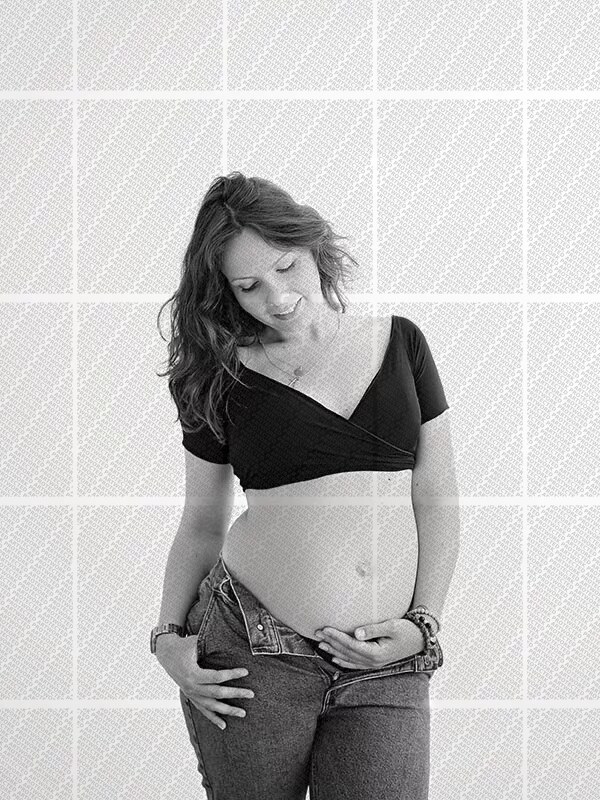 Femme enceinte souriante en pantalon jean et top court, posant tendrement la main sur son ventre rond
