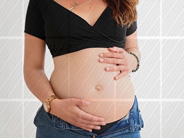 Femme enceinte habillée d'un haut noir et d'un jean tenant son ventre à deux mains