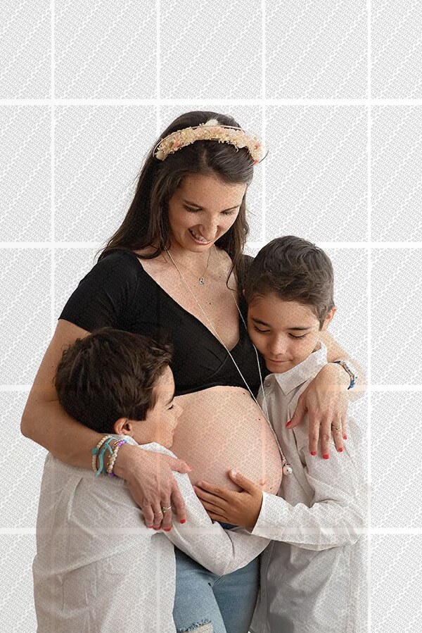 Femme enceinte souriante entourée de ses deux jeunes garçons qui touchent son ventre avec tendresse
