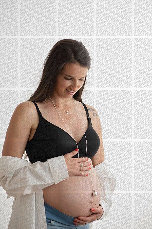 Femme enceinte souriante portant un soutien-gorge noir et une chemise blanche ouverte, caressant son ventre arrondi