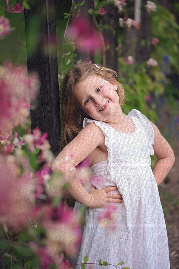 Petite fille souriante en robe blanche posant dans un jardin fleuri avec des mains sur les hanches