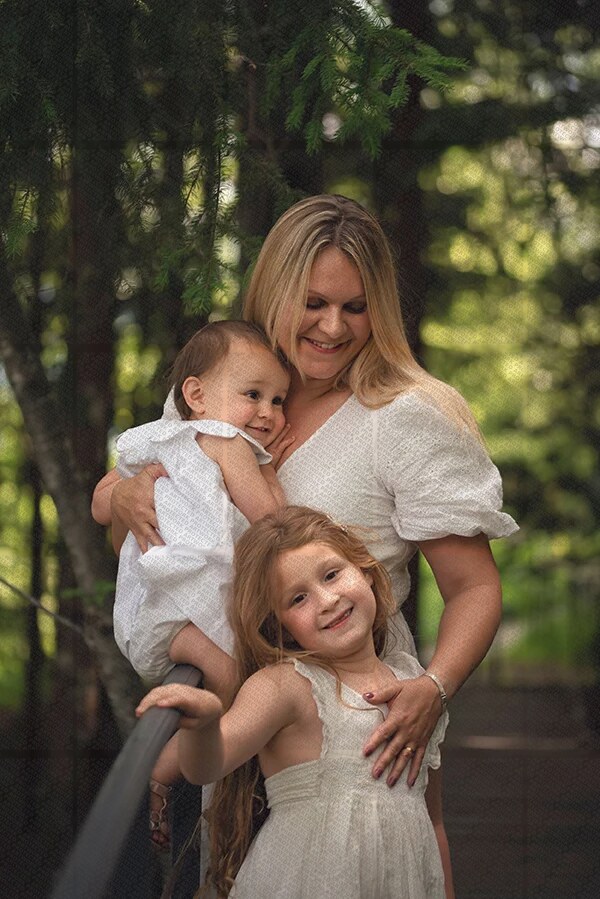 Mère souriante avec ses deux filles, dans un cadre naturel verdoyant, en tenue blanche assortie