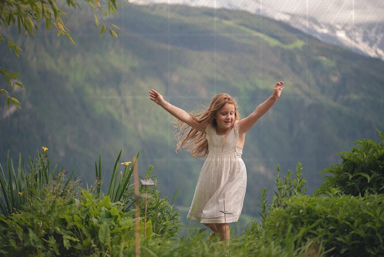 Jeune fille souriante en robe blanche jouant dans un jardin fleuri avec montagnes en arrière-plan