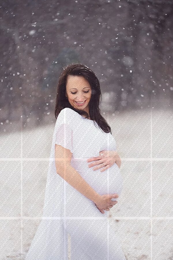 Femme enceinte souriante en robe blanche tenant son ventre sous une chute de neige