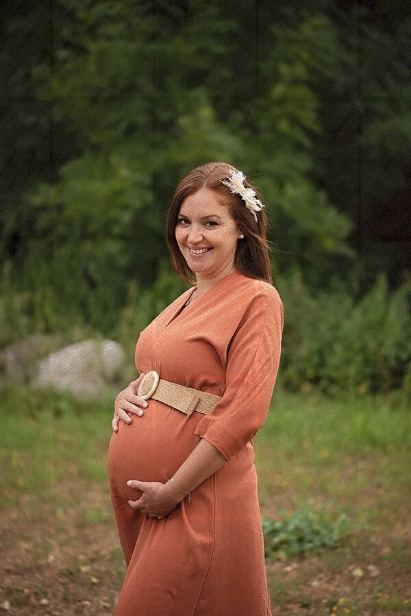 Femme enceinte souriante en robe orange posant en plein air dans un cadre naturel verdoyant