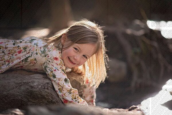 Enfant souriante allongée sur un rocher en pleine nature, vêtue d'une robe fleurie, lumière douce
