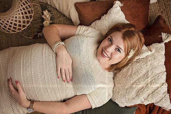 Femme enceinte souriante allongée sur des coussins dans un cadre chaleureux et naturel