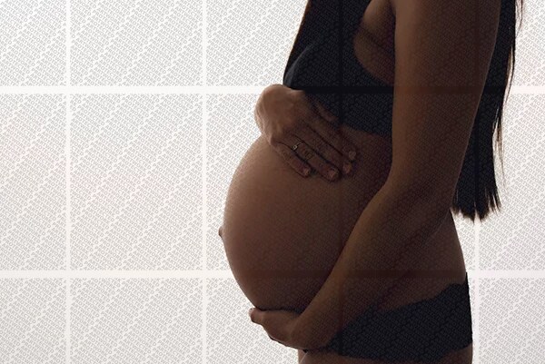 Profil d'une femme enceinte en sous-vêtements noirs tenant son ventre arrondi avec ses mains
