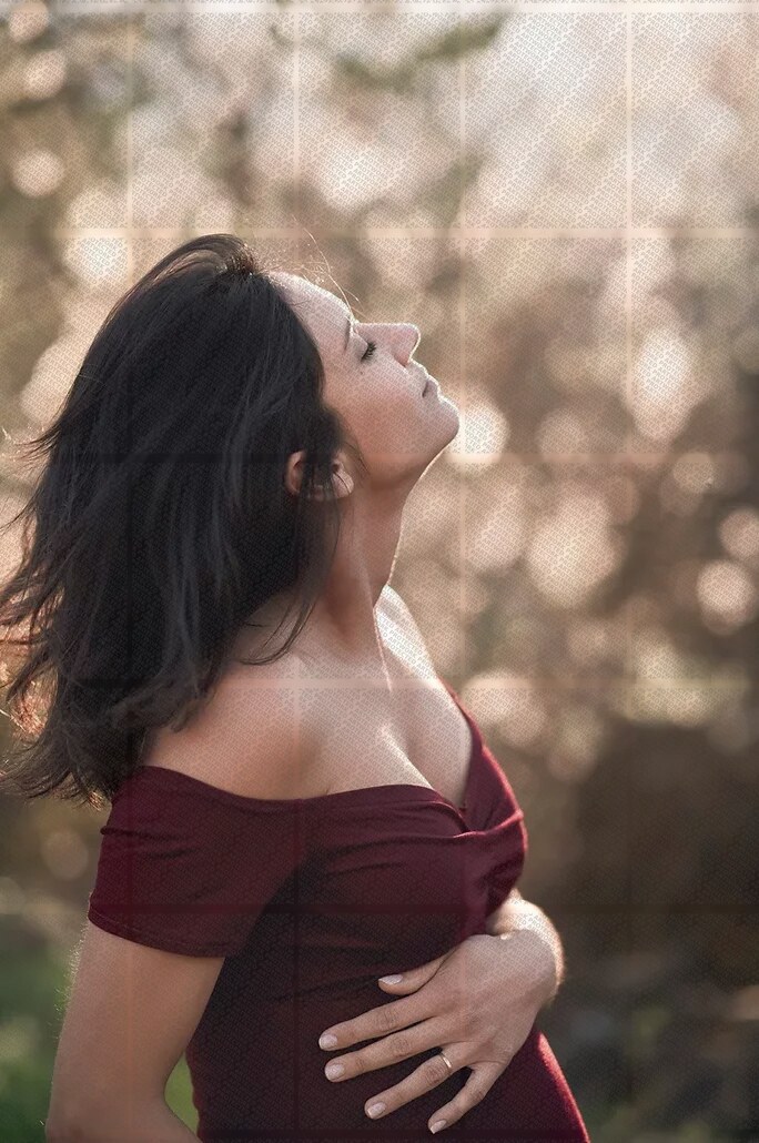 Portrait d'une femme enceinte de profil, main posée sur son ventre, lumière douce en extérieur
