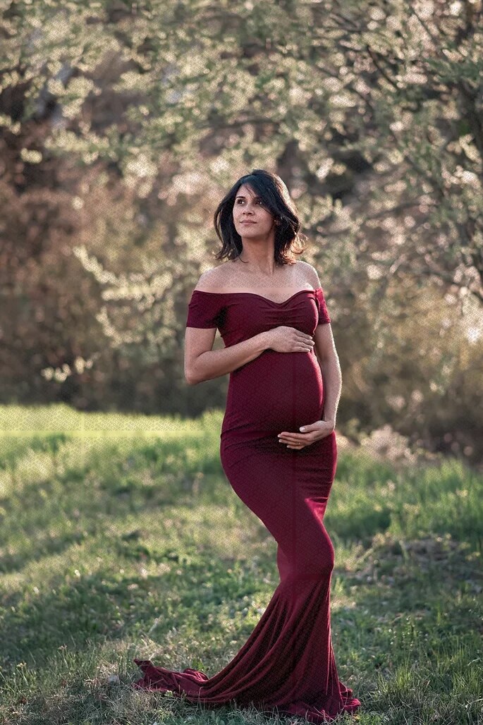 Femme enceinte en robe bordeaux élégante posant dans un jardin ensoleillé au printemps