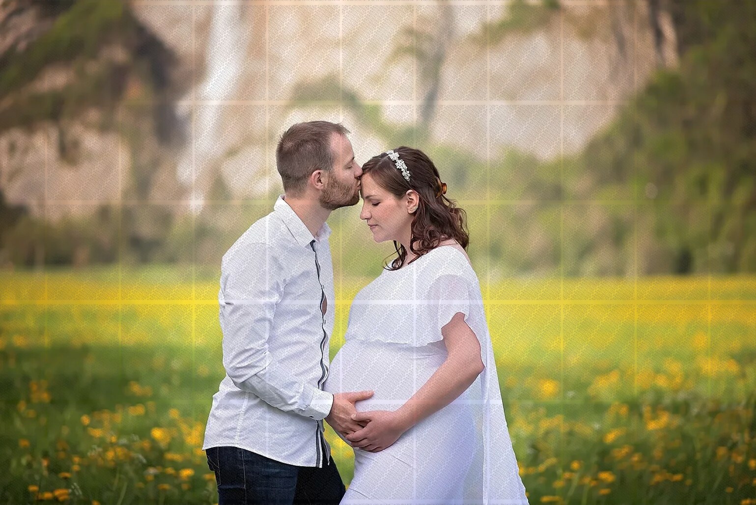 Couple dans un champ fleuri, l'homme embrasse le front de la femme enceinte habillée en blanc