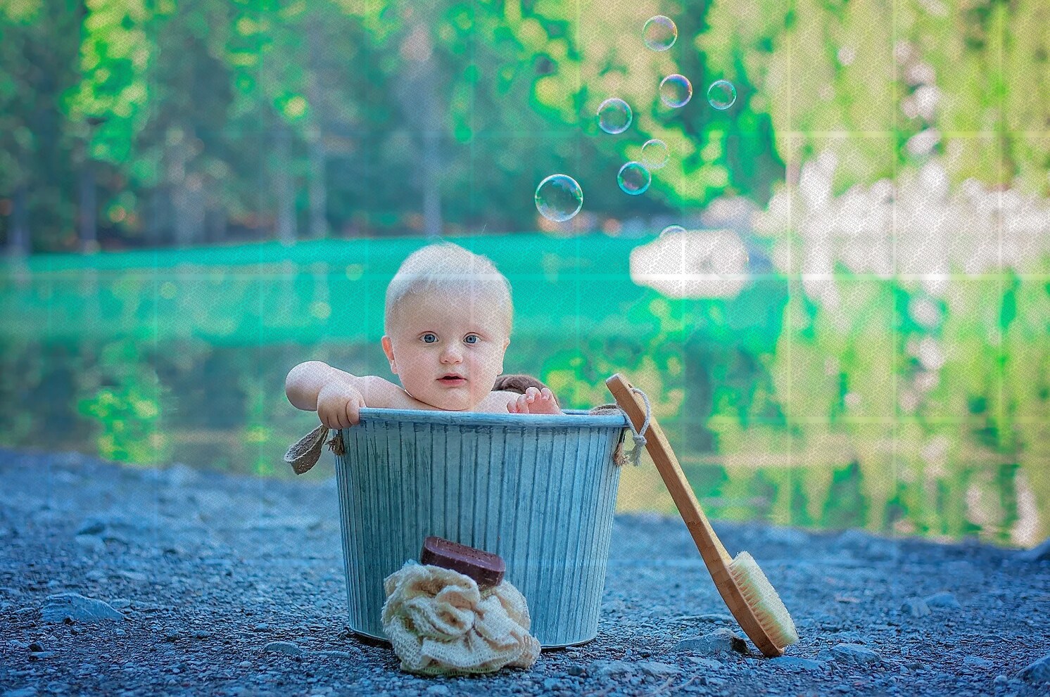 Bébé dans un seau en métal posé au bord d'un étang avec bulles flottantes en arrière-plan