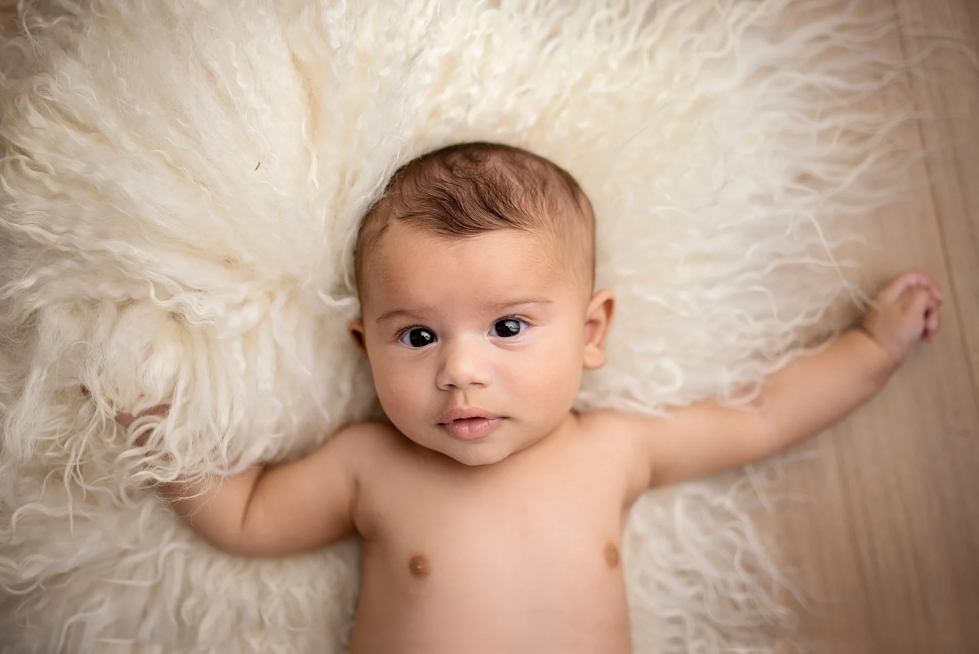 Bébé allongé sur une peau de mouton blanche aux poils longs regardant l'objectif