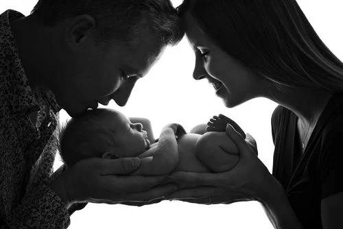 Parents souriants tenant et regardant tendrement leur bébé nouveau-né dans une ambiance douce en noir et blanc